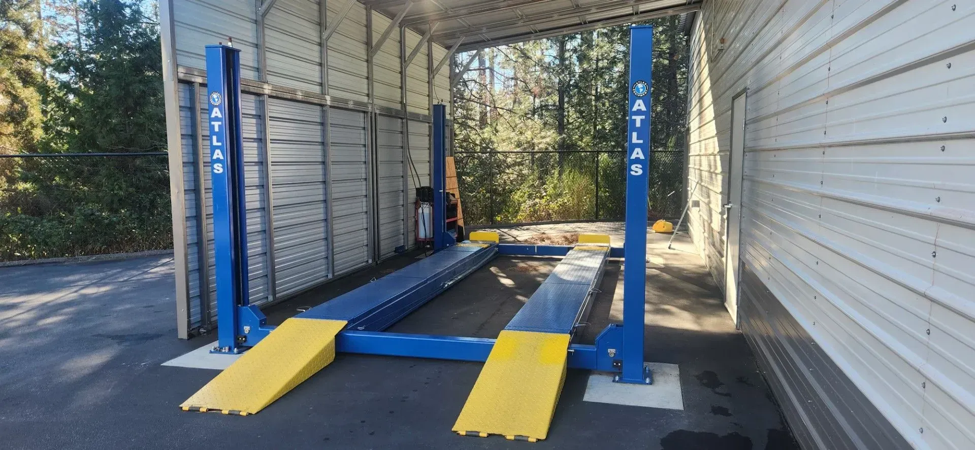 Blue two-post vehicle lift with yellow ramps in an outdoor garage bay | Tripp's Auto Body