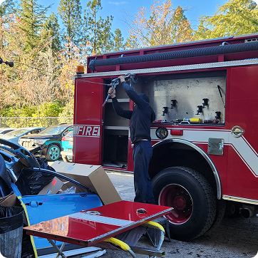 Fire truck scene with firefighter loading equipment at an open side compartment after a roadside incident | Tripp's Auto Body