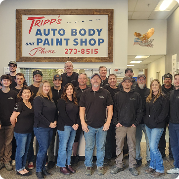 Group of auto body shop employees posing indoors beneath a 