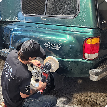Person polishing the rear of a green SUV with a power buffer in a driveway | Tripp's Auto Body