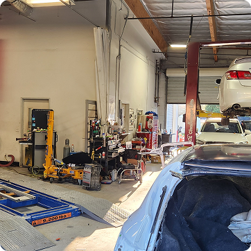 Auto repair garage with a car on a lift, tools, and equipment scattered around the workshop. | Tripp's Auto Body