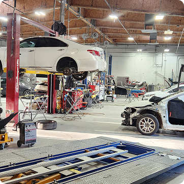 Auto repair shop with a white car lifted on a hoist and another car under repair on the right | Tripp's Auto Body