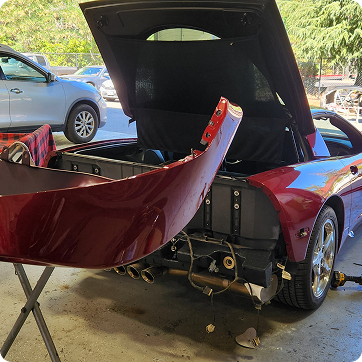 Rear view of a red sports car with its bumper removed and trunk open, parked in a driveway. | Tripp's Auto Body