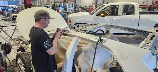Man working on a car body frame in a garage, with tools and vehicles in the background | Tripp's Auto Body