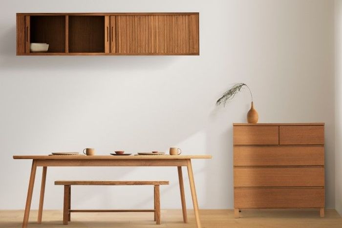 Minimal wooden dining room with table, bench, wall shelf, and dresser against a neutral wall