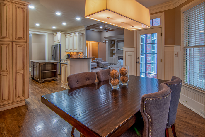 Dining room with dark wood table, upholstered chairs, and a large hanging light, opening to a kitchen.