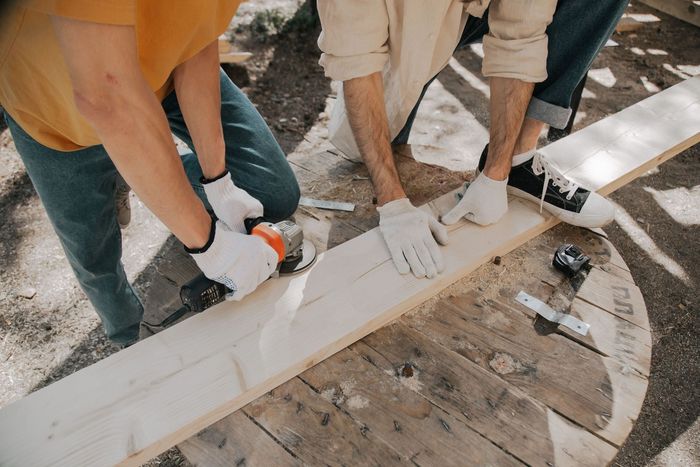Three people painting a white wooden plank on a construction site floor