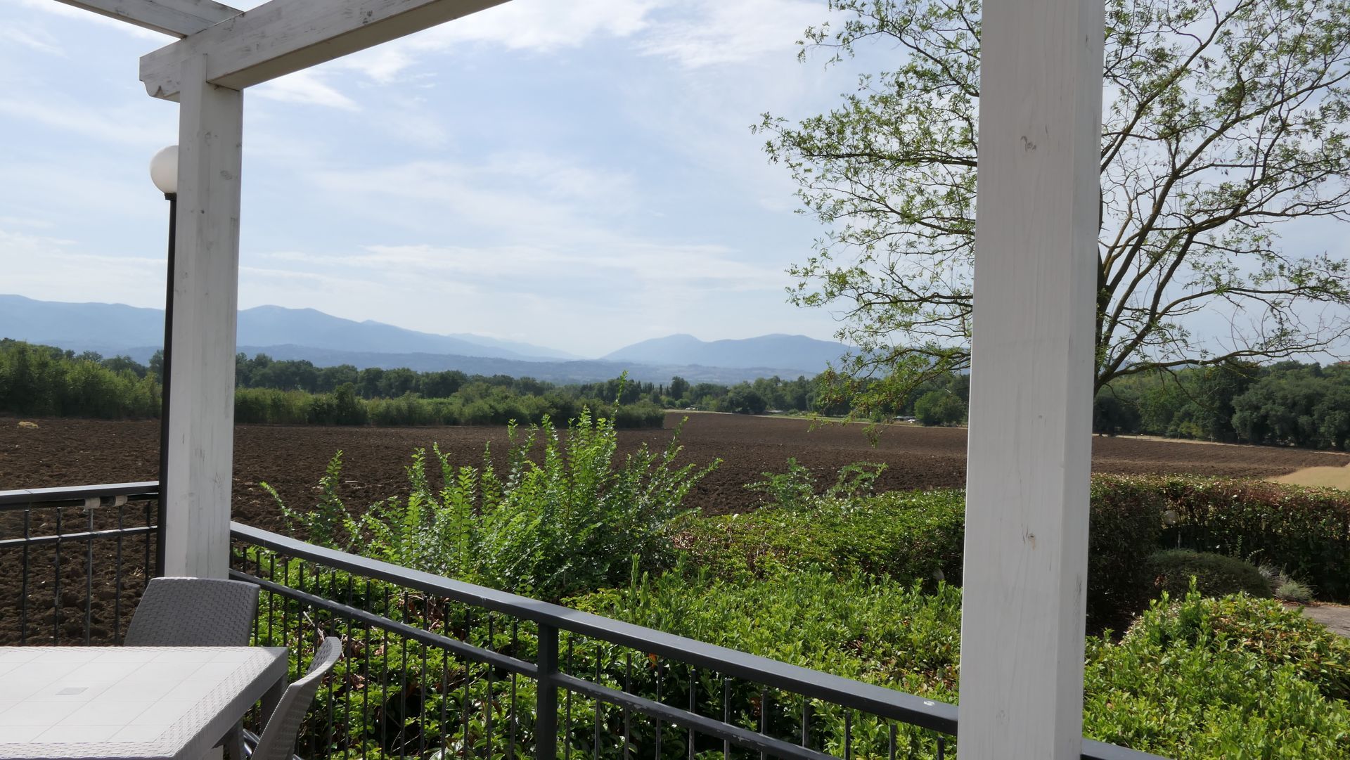 Patio coperto con vista sul giardino verde, sulle colline in lontananza e su un cielo nuvoloso.