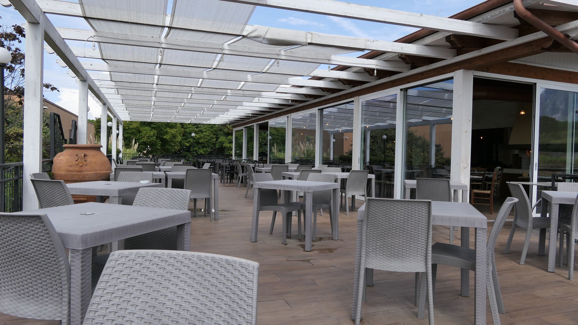 Terrazza esterna del ristorante con sedie e tavoli grigi sotto una pergola bianca.