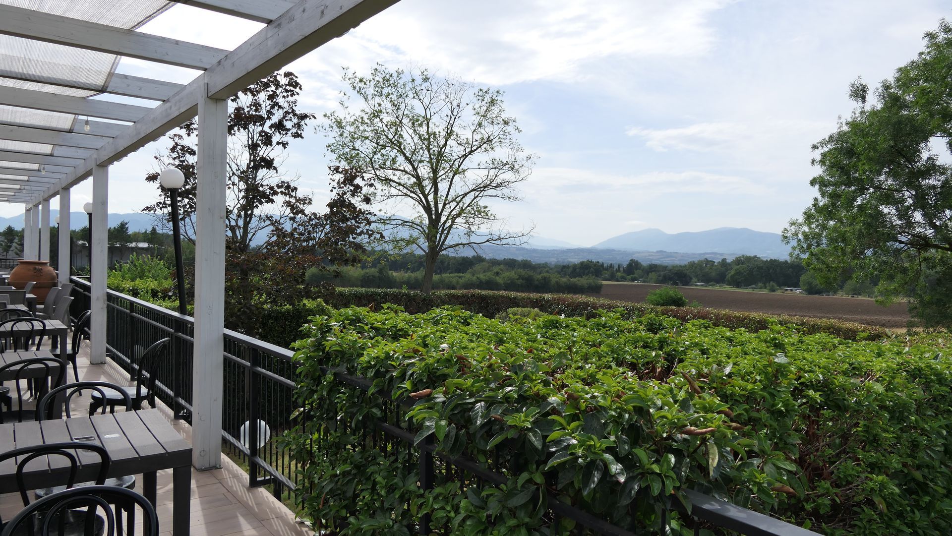 Terrazza coperta con vista sul verde lussureggiante e sulle colline in lontananza, sotto un cielo nuvoloso.