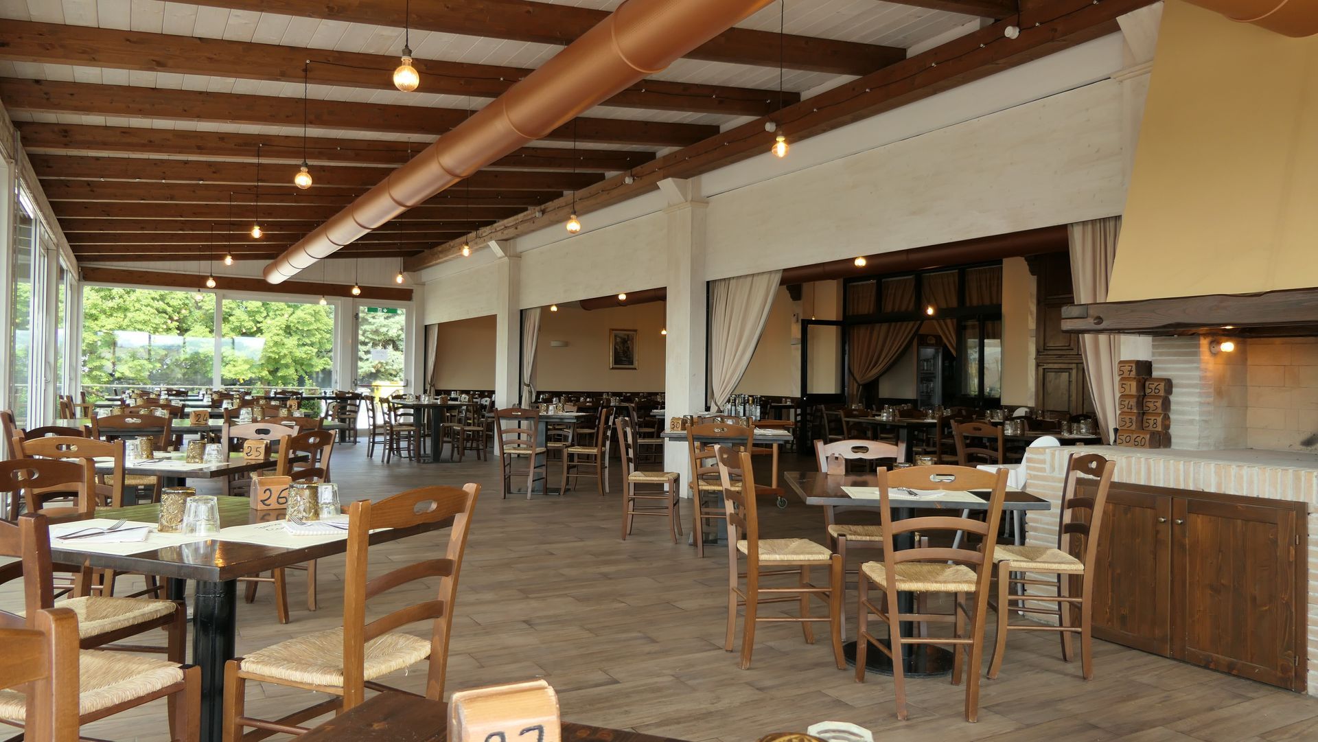 Sala da pranzo all'aperto con tavoli e sedie in legno e luci soffuse dai toni caldi.