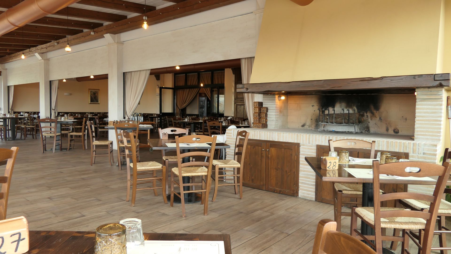 Sala da pranzo rustica del ristorante con tavoli e sedie in legno sotto un soffitto con travi inclinate.