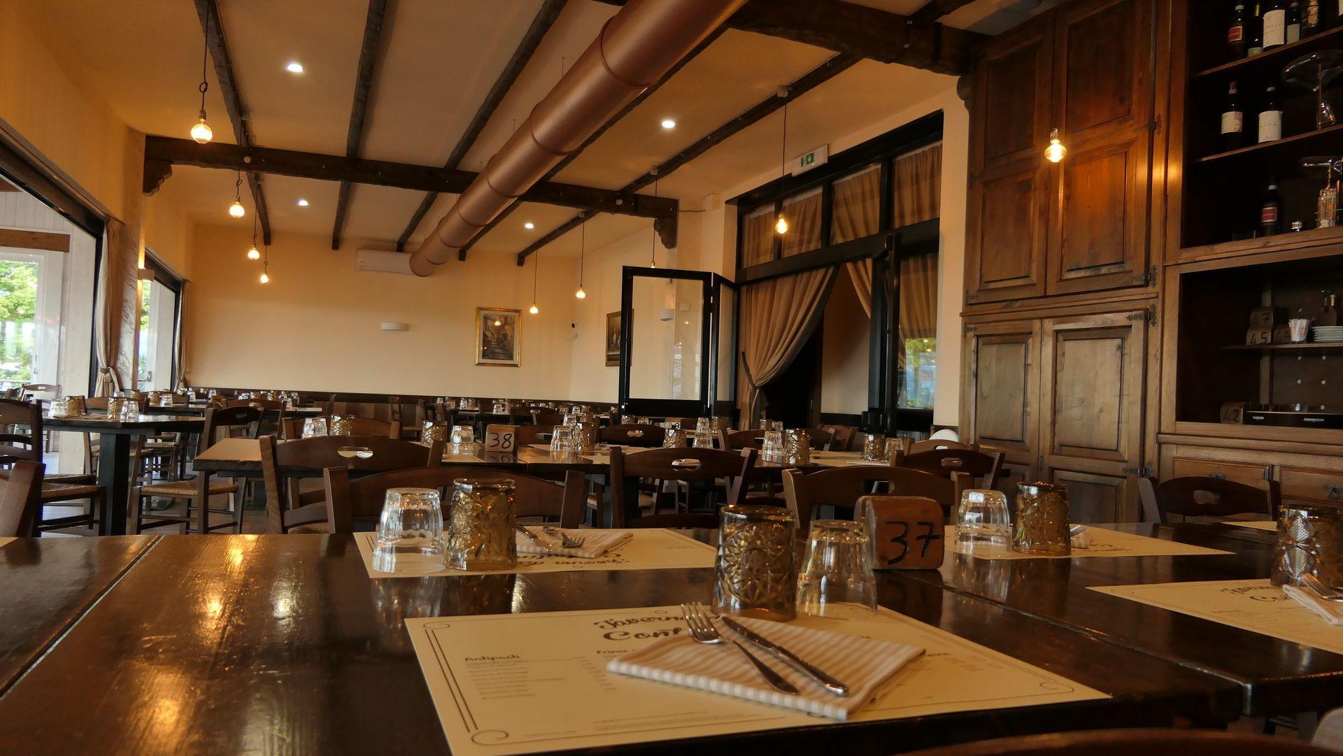 Accogliente sala da pranzo del ristorante con tavoli in legno, lampade a sospensione e apparecchiatura della tavola.