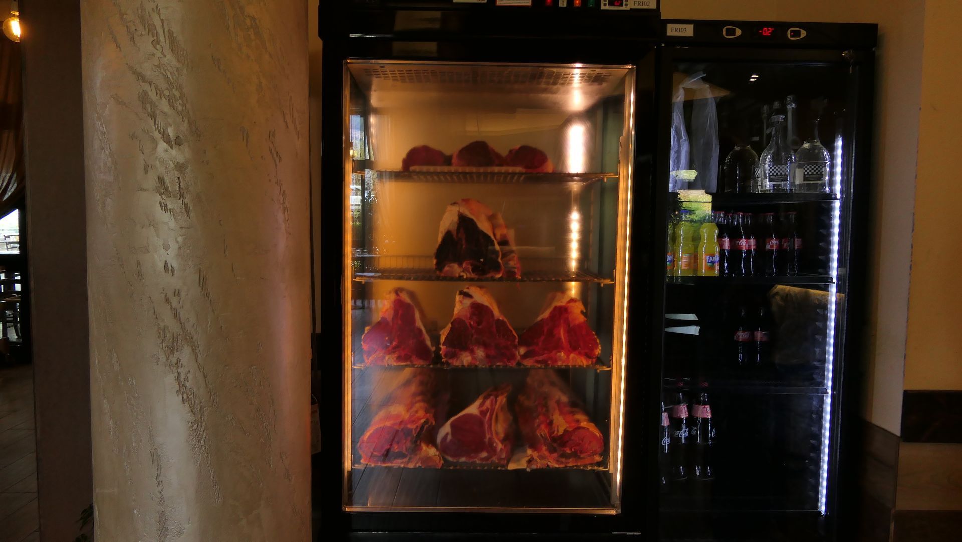 Vetrina espositiva con pasticcini o decorazioni rosse illuminate, accanto a un refrigeratore per bevande scuro.