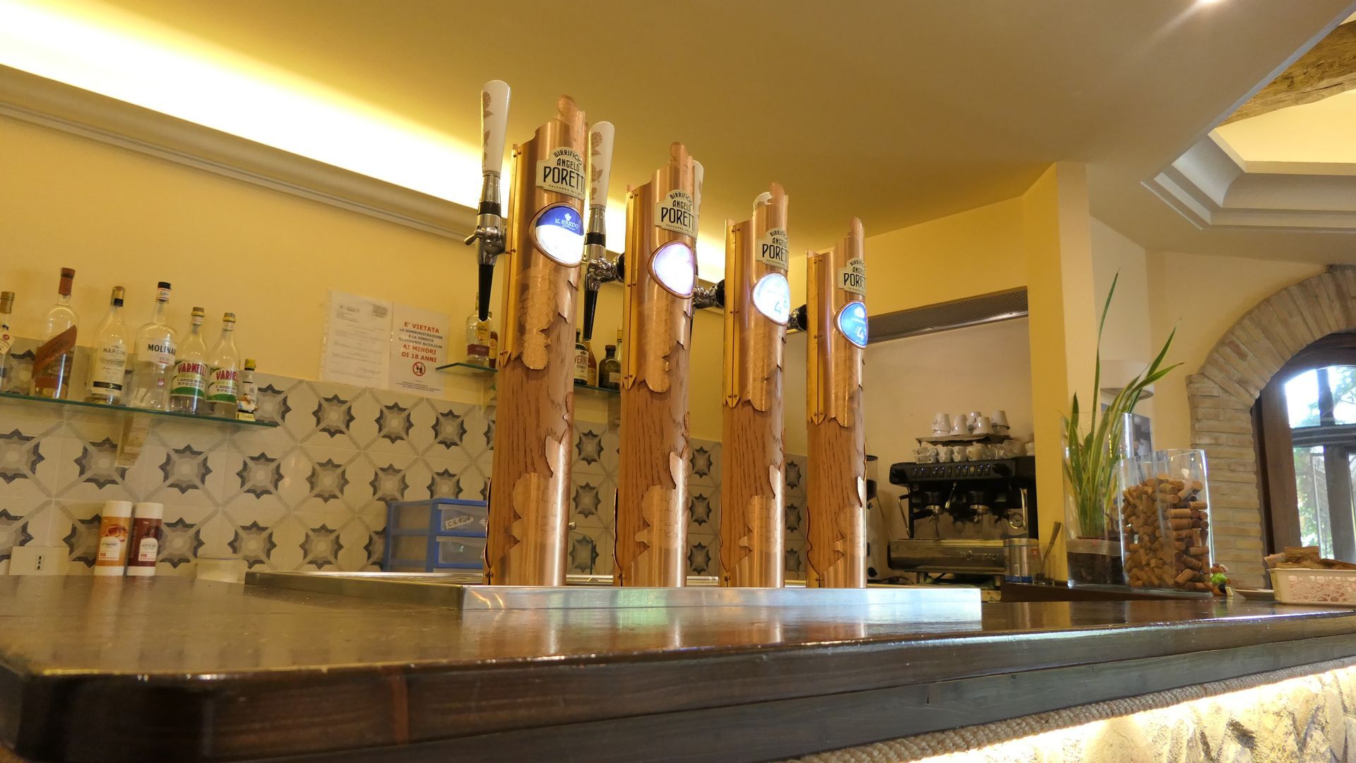 Rubinetti di birra in legno allineati sul bancone di un pub illuminato da una luce calda.