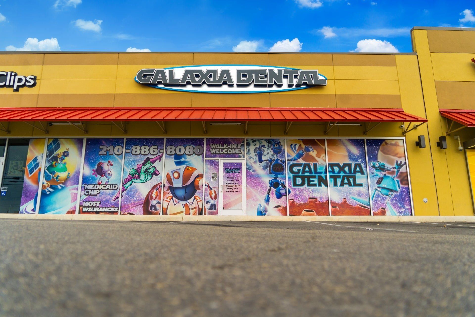 Storefront with bright yellow facade and colorful posters reading “Galacta Dental” on a sunny day