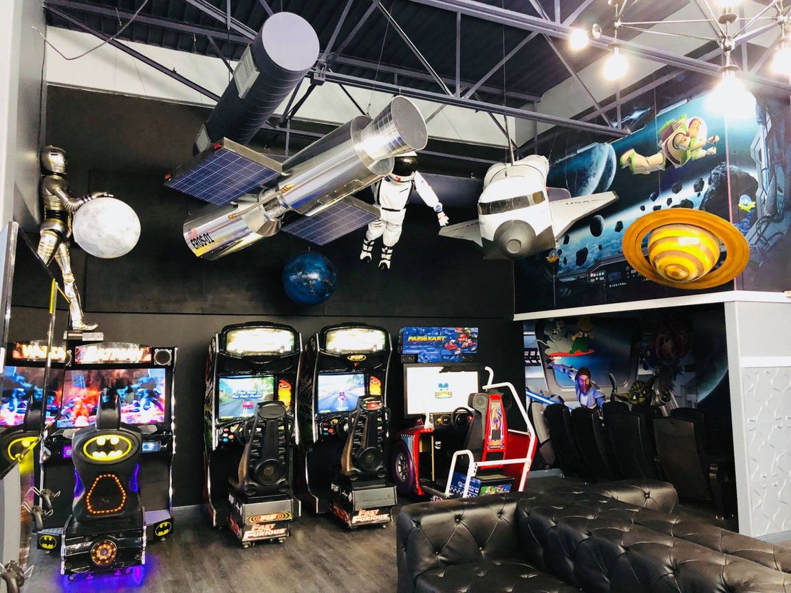 Arcade with rows of arcade cabinets, a black couch, and spaceship-themed ceiling decor