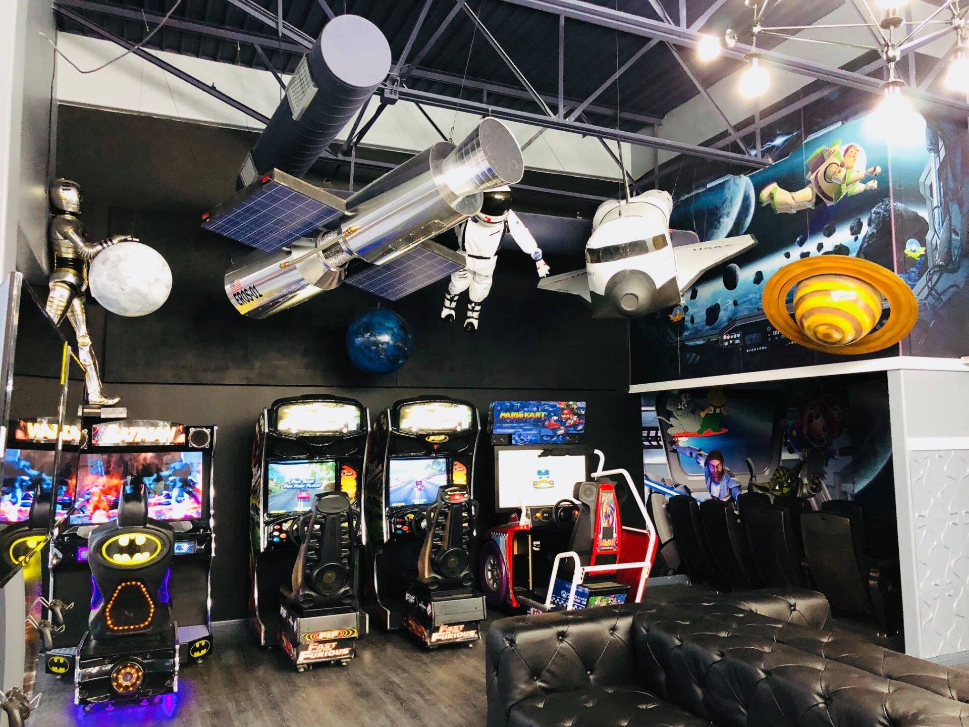 Arcade with rows of arcade cabinets, a black couch, and spaceship-themed ceiling decor