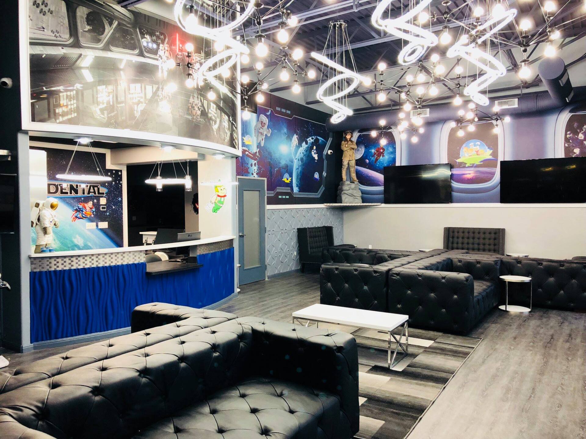 Dim lounge with black sofas, blue curtains, neon ceiling lights, and a bar-style counter.