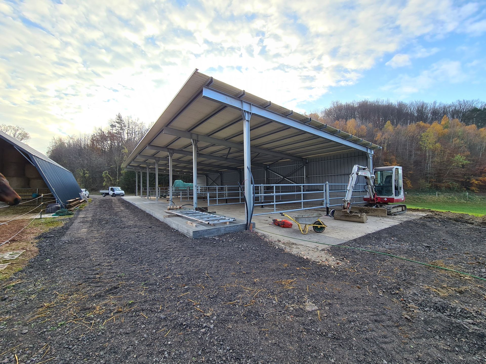 Auf einem Feld wird eine offene Metallkonstruktion im Bau befindlich. Ein Bagger ist anwesend.