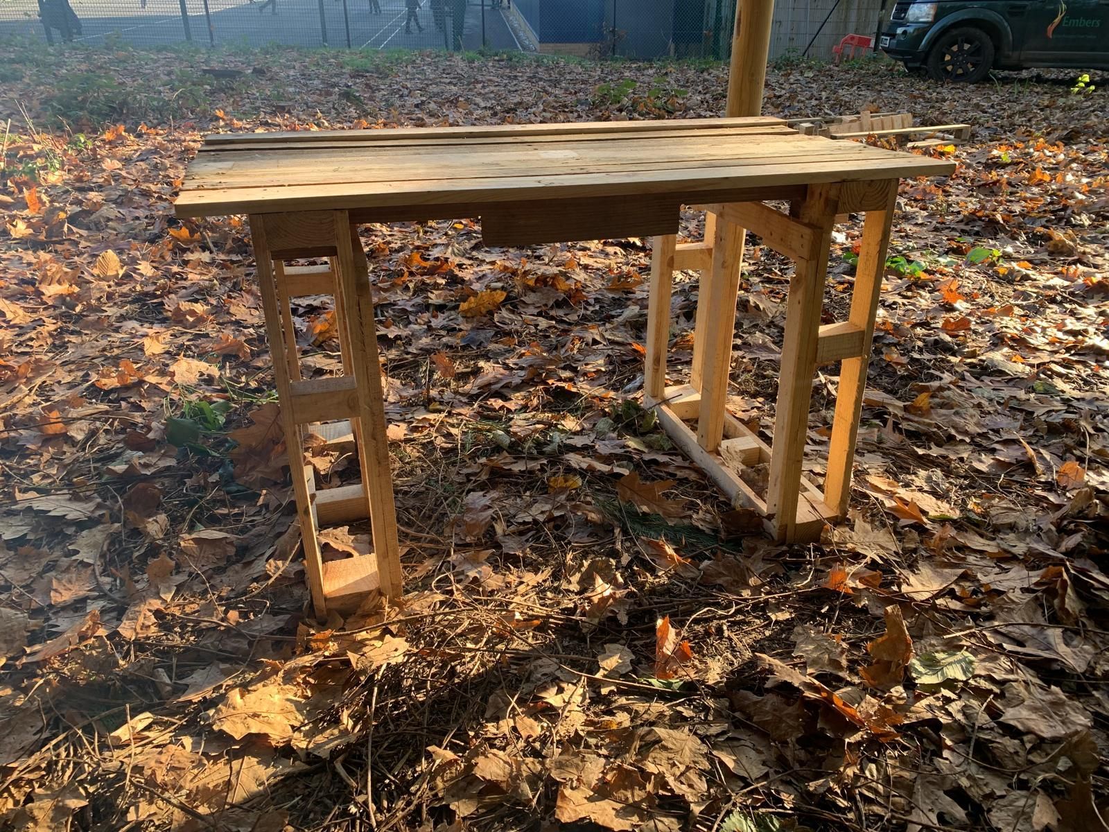 A wooden table is sitting in the middle of a pile of leaves.
