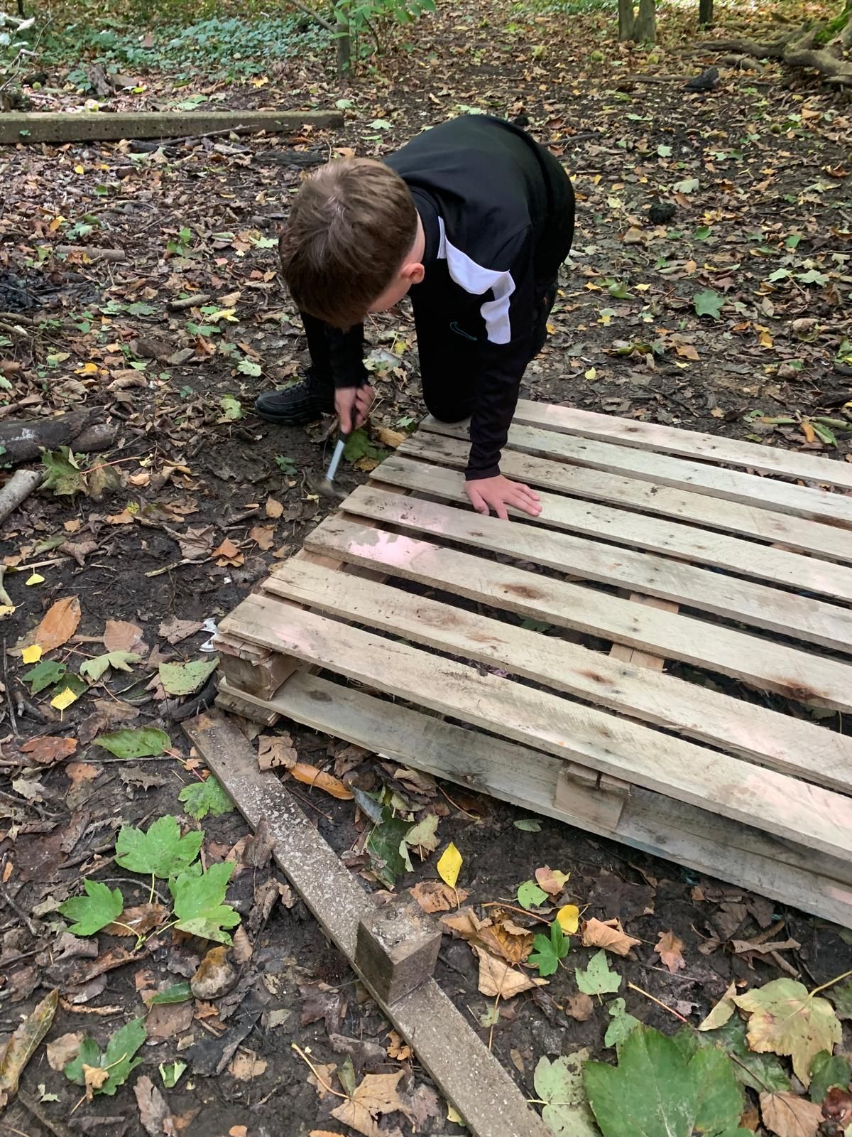 A young boy is kneeling on a wooden pallet in the woods.