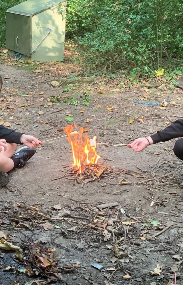 Two people are sitting around a fire in the dirt.
