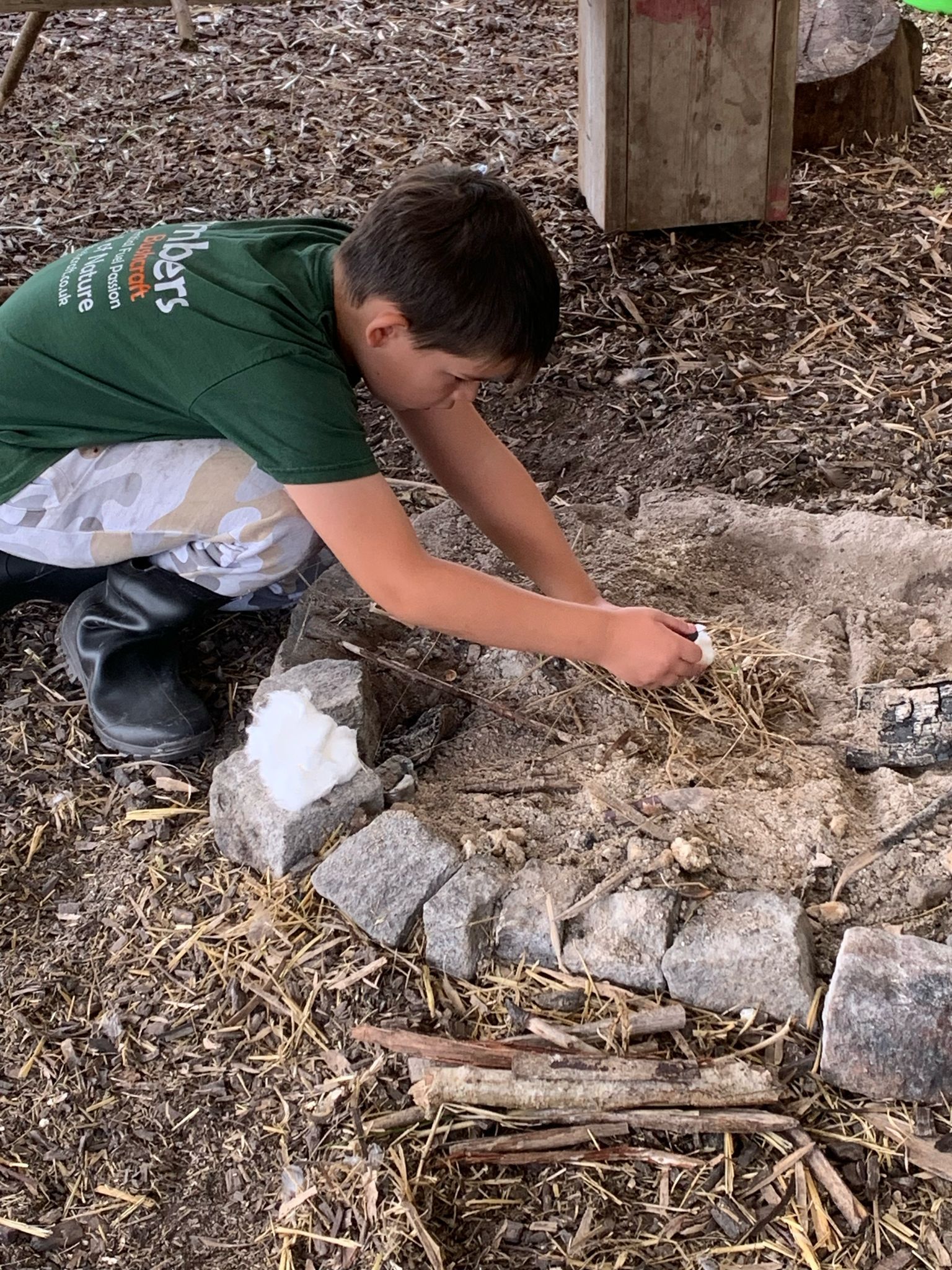 A young boy in a green top is building a fire.