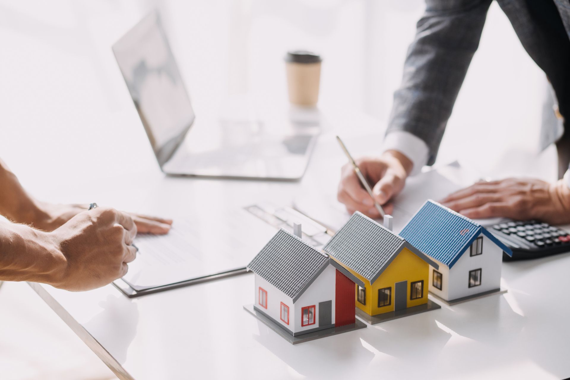Person signing documents with miniature houses and calculator on a desk