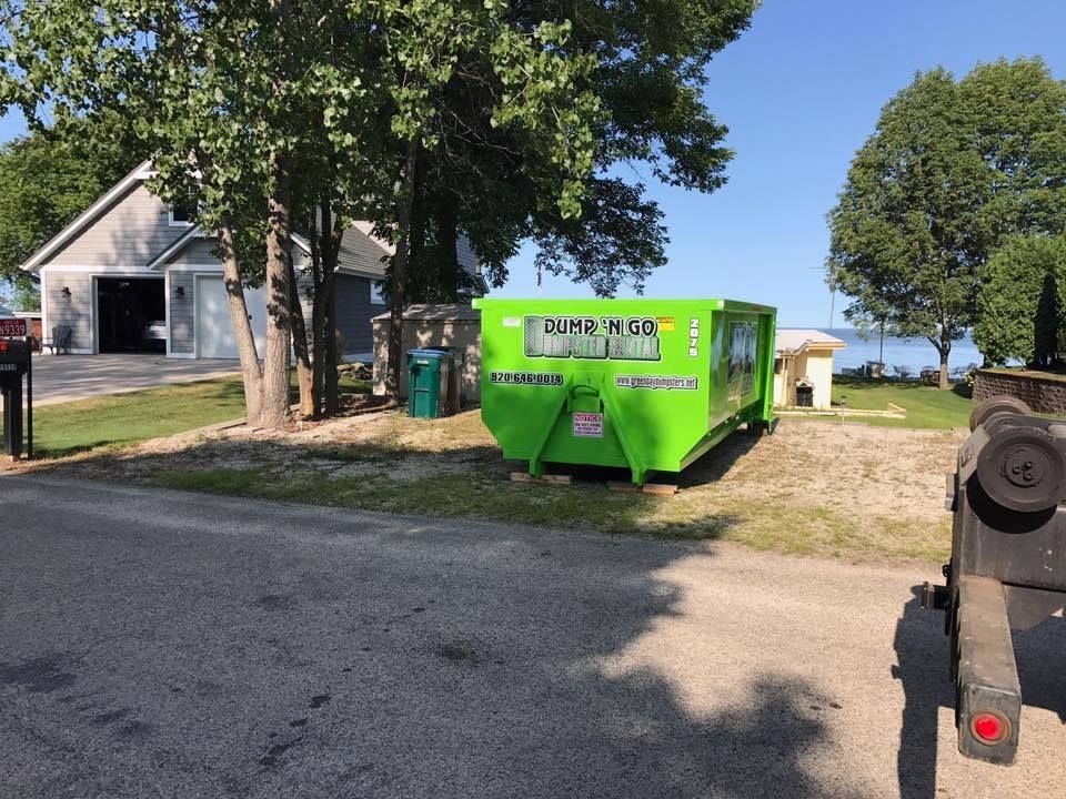 Bright green dumpster near a house and trees beside a lakeside road