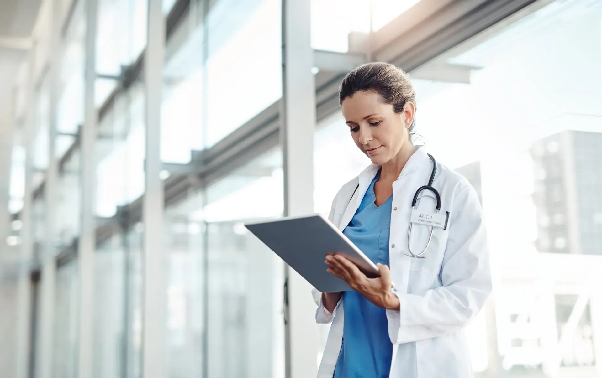 A female doctor is looking at a tablet in a hospital hallway. A female doctor is looking at a tablet in a hospital hallway.