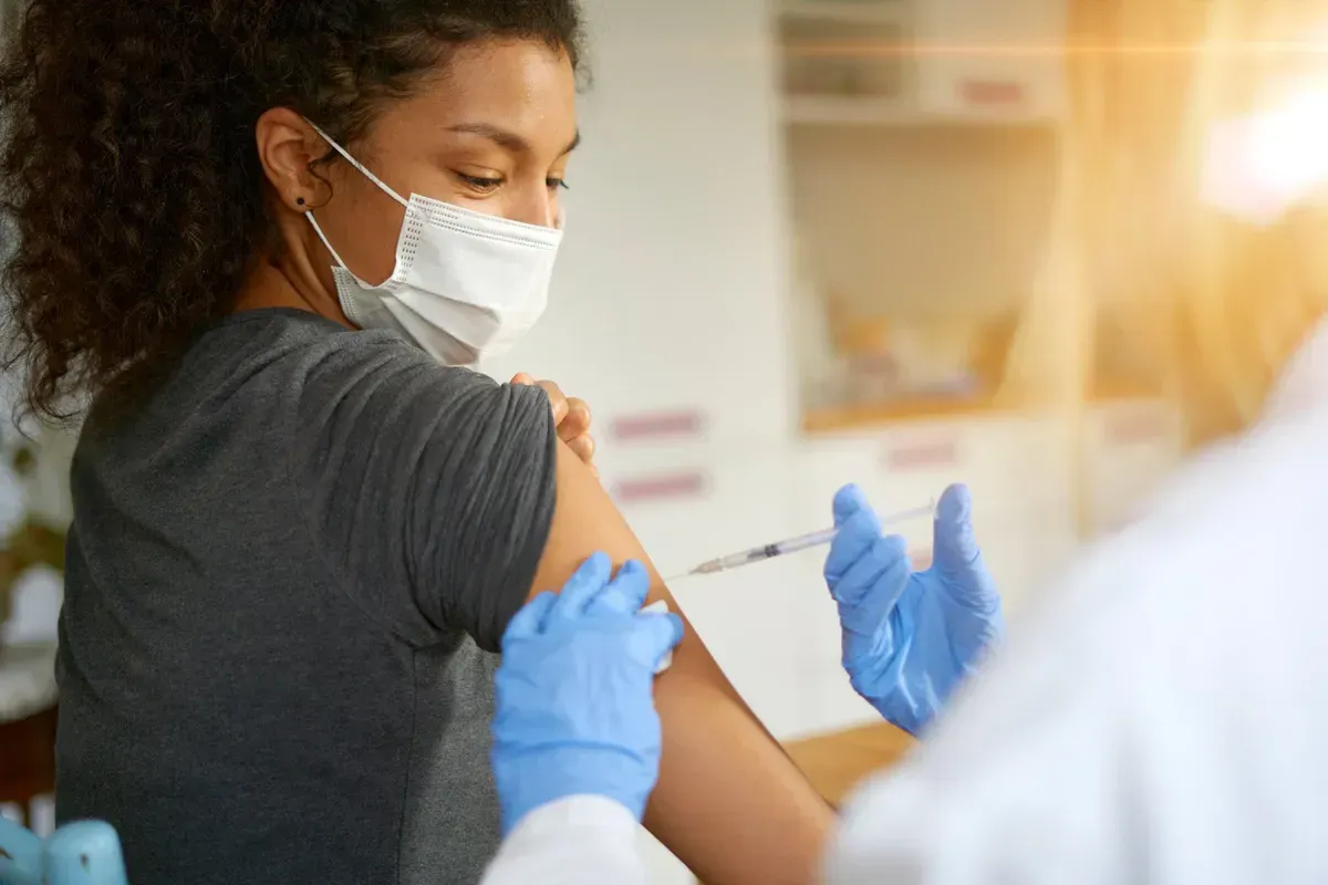 A woman wearing a mask is getting a vaccine in her arm.