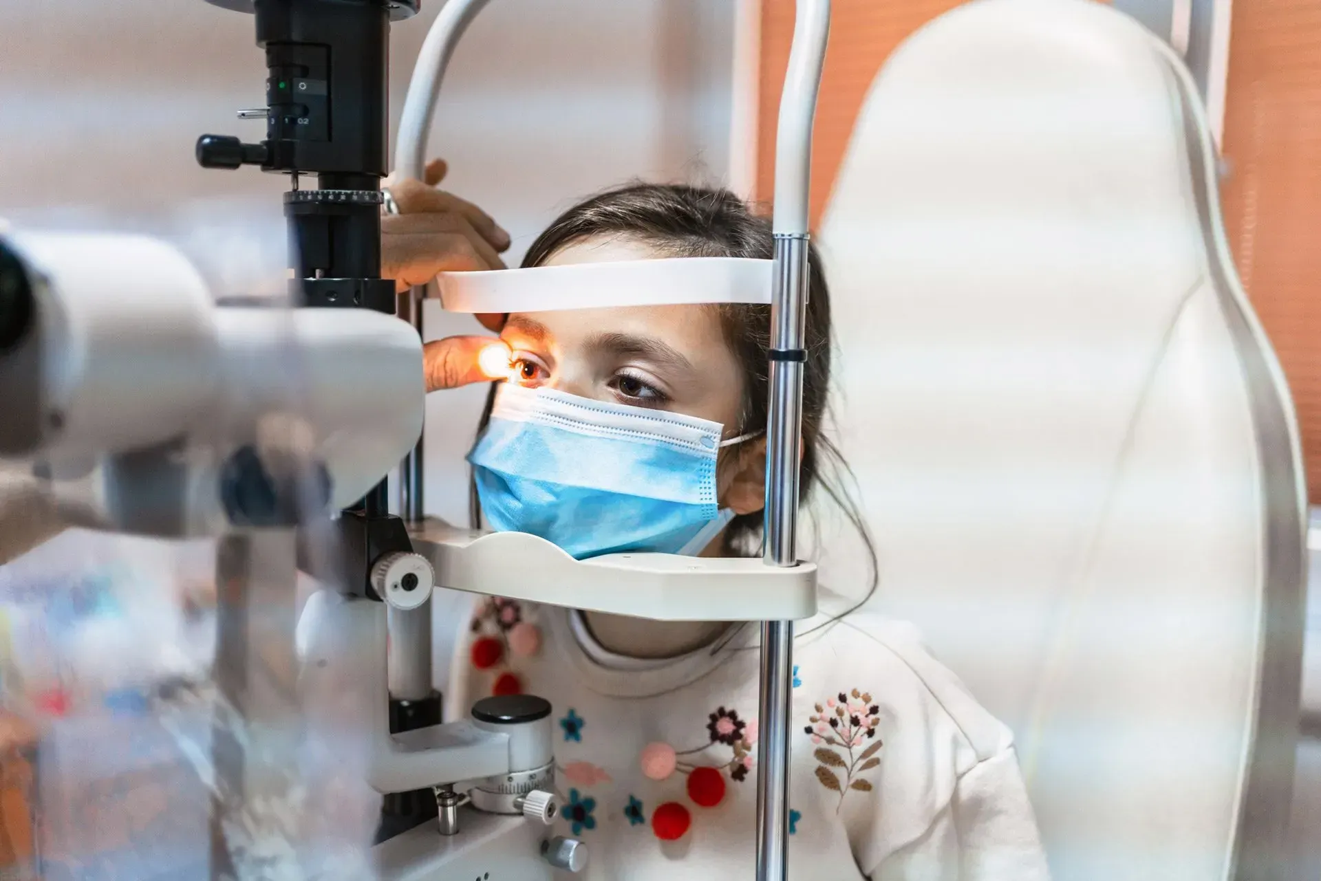 A woman wearing a mask is getting her eyes examined by an ophthalmologist. A woman wearing a mask is getting her eyes examined by an ophthalmologist.