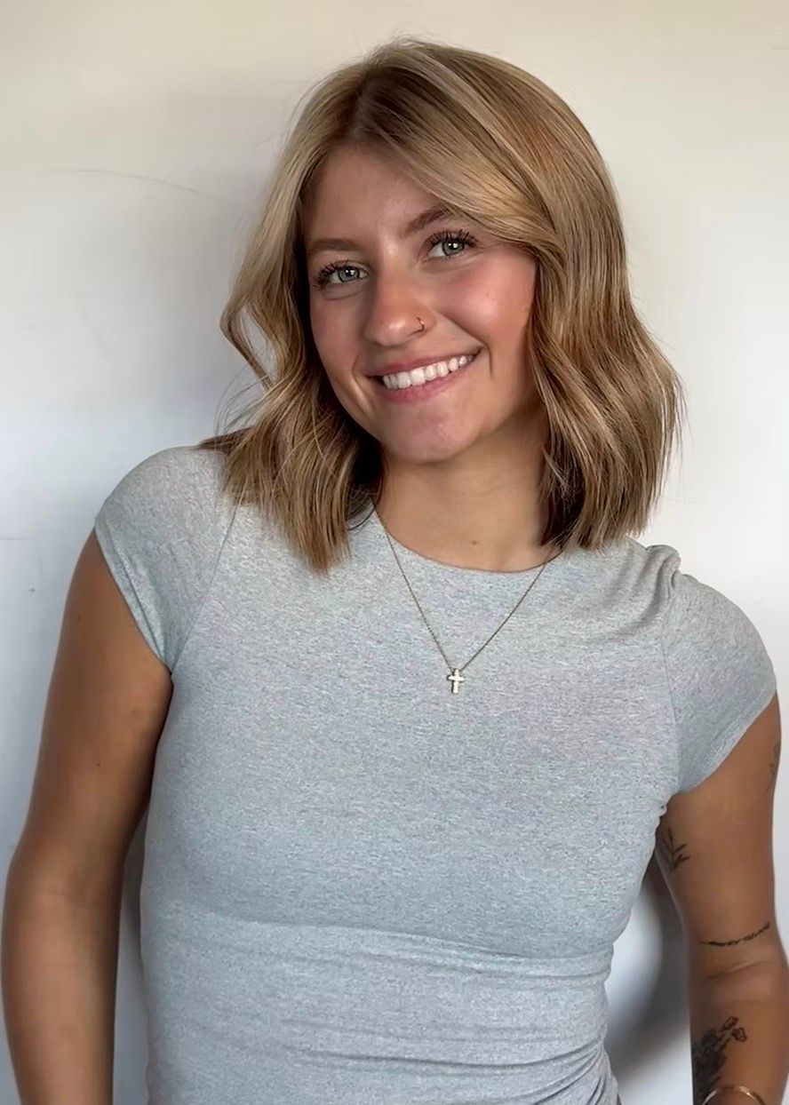 Blonde woman with blue eyes smiles. Wears blue top, hair has sparkle accents. Black background.