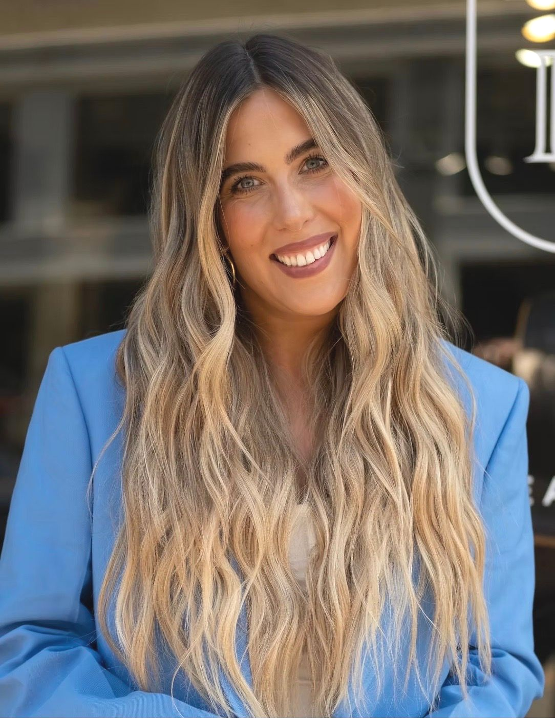 Woman with long blonde hair smiles in a light blue blazer.