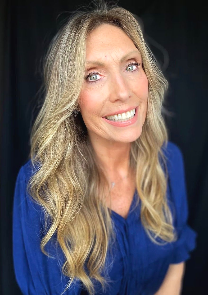 Smiling woman with long wavy blonde hair in a blue top against a black background