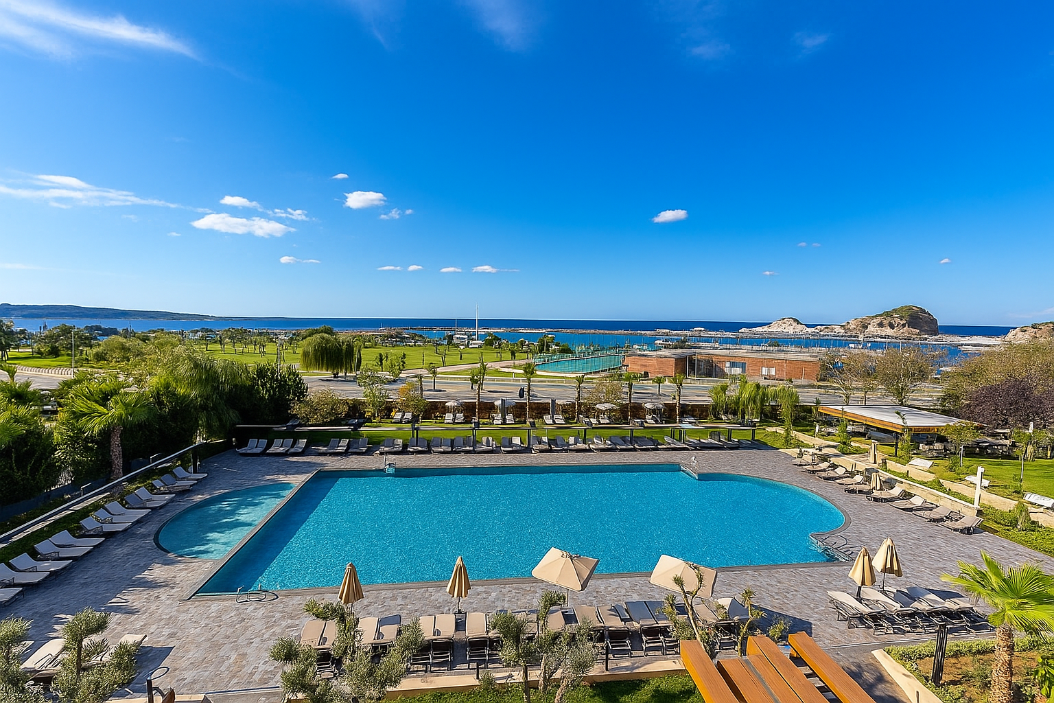 Resort pool with umbrellas and lounge chairs overlooking a bright blue bay under a clear sky