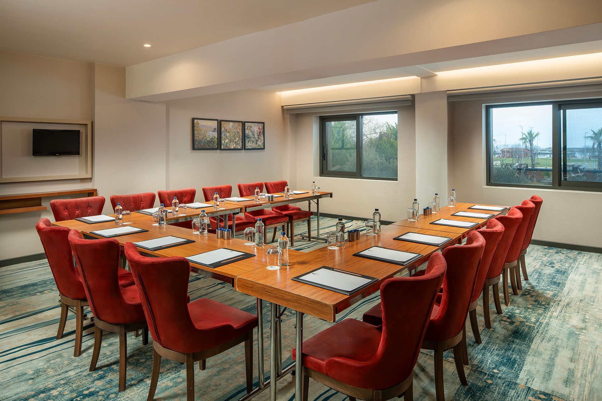 Conference room with U-shaped table setup, red chairs, and windows overlooking a city view.