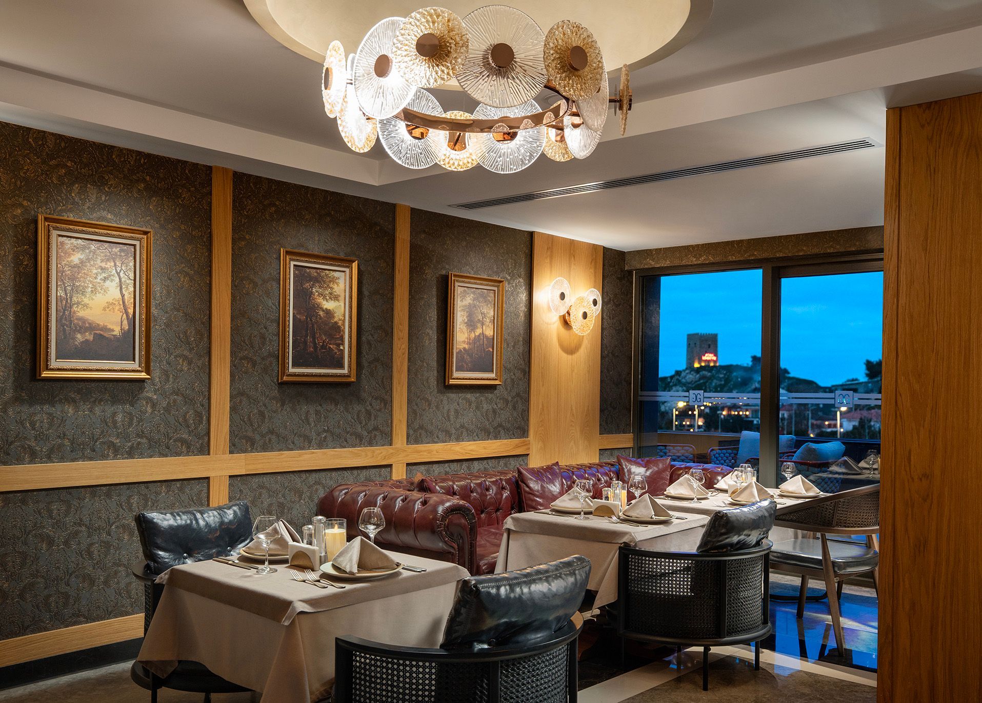 Elegant restaurant dining room with set tables, framed wall art, and a window view at dusk