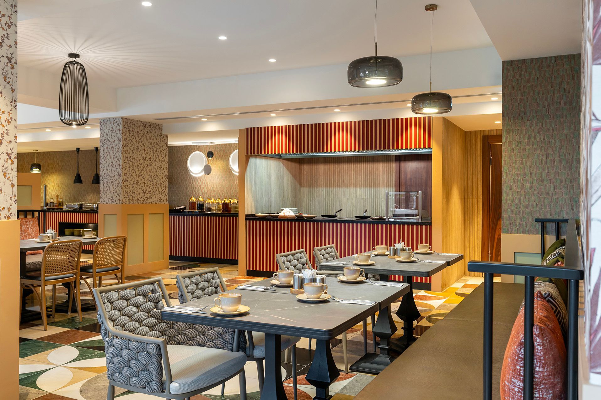 Modern restaurant dining area with patterned chairs, tables set for service, and a wood-accented buffet counter