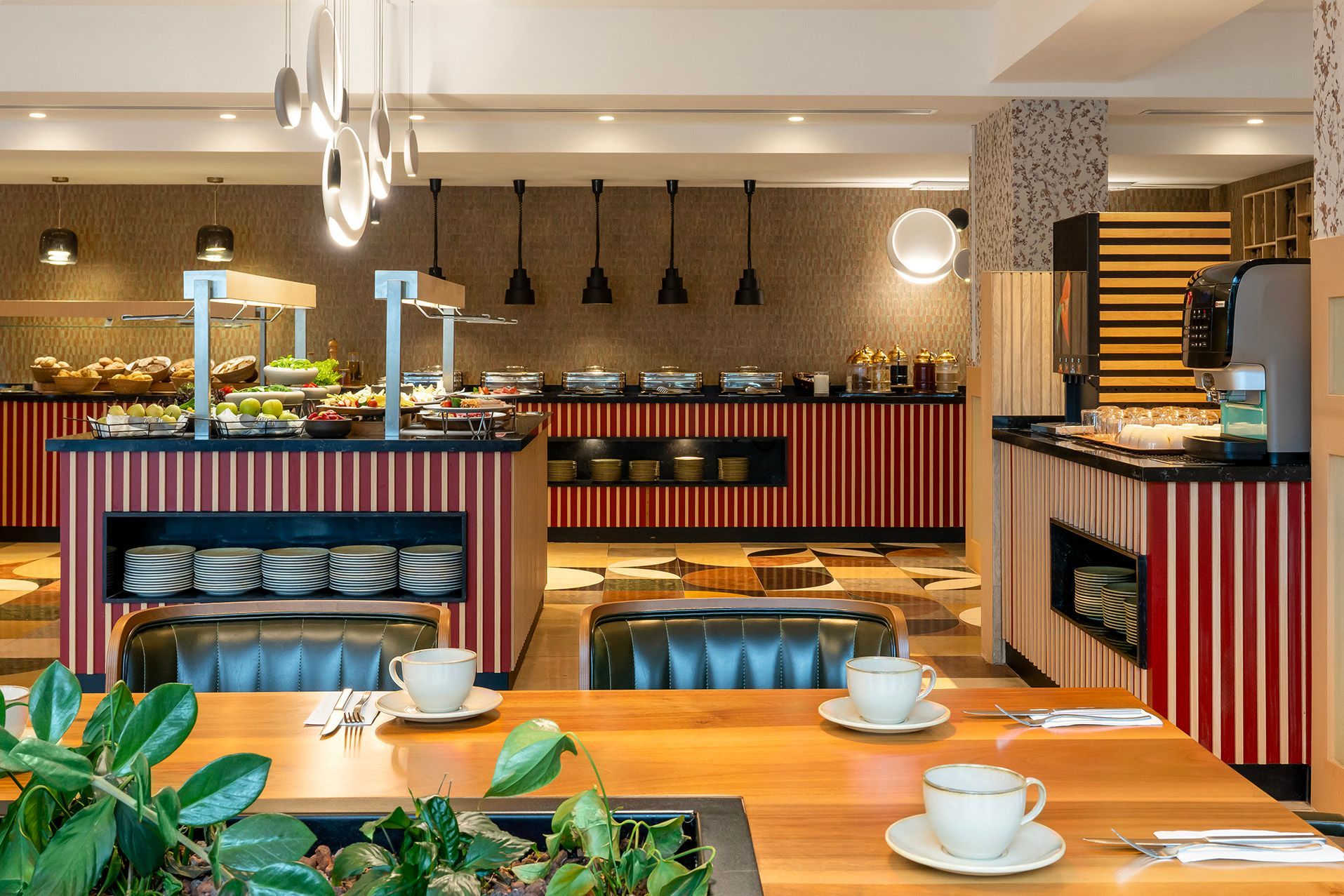 Bright buffet dining room with red striped counters, hanging lights, and tables set with white cups