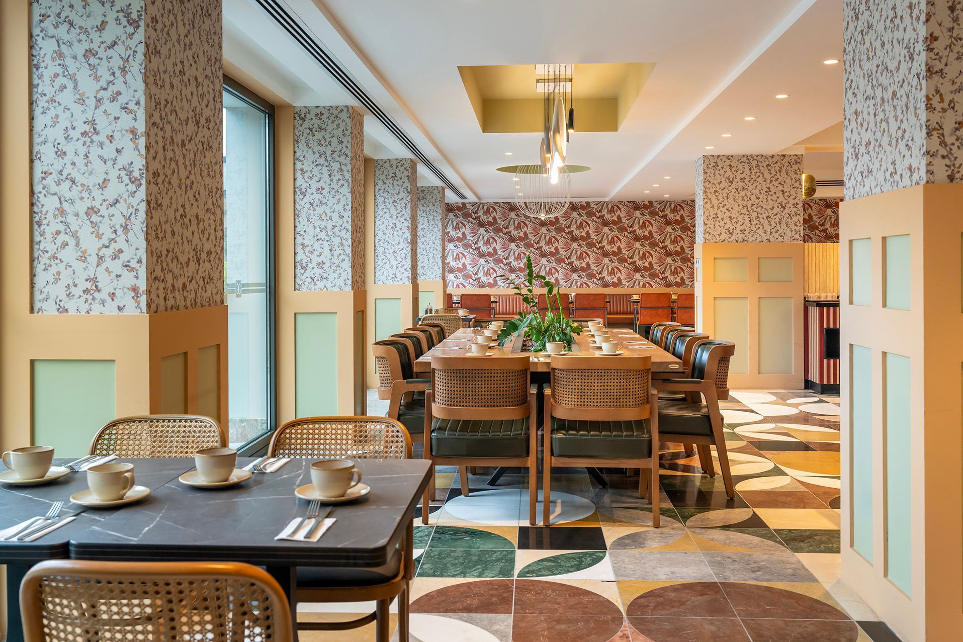 Bright, modern dining room with wicker chairs, patterned walls, and tables set for guests.