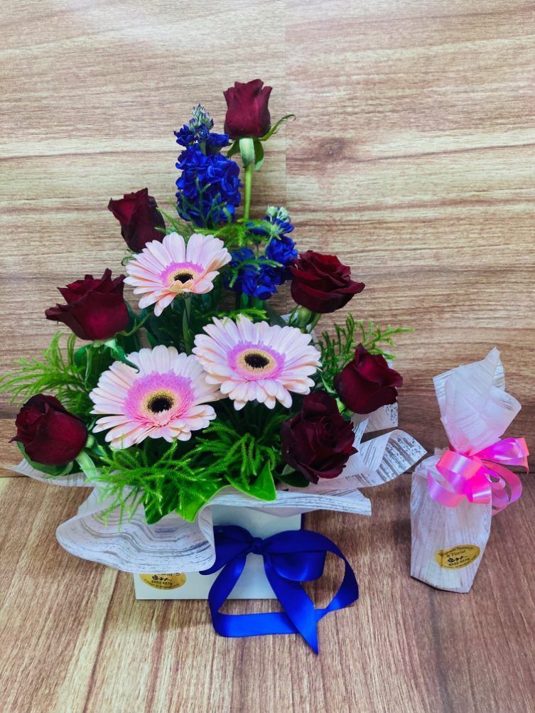 A Bouquet of Flowers in a Vase With a Blue Ribbon on a Wooden Table — Wingham Nursery and Florist PTY Ltd In Wingham, NSW
