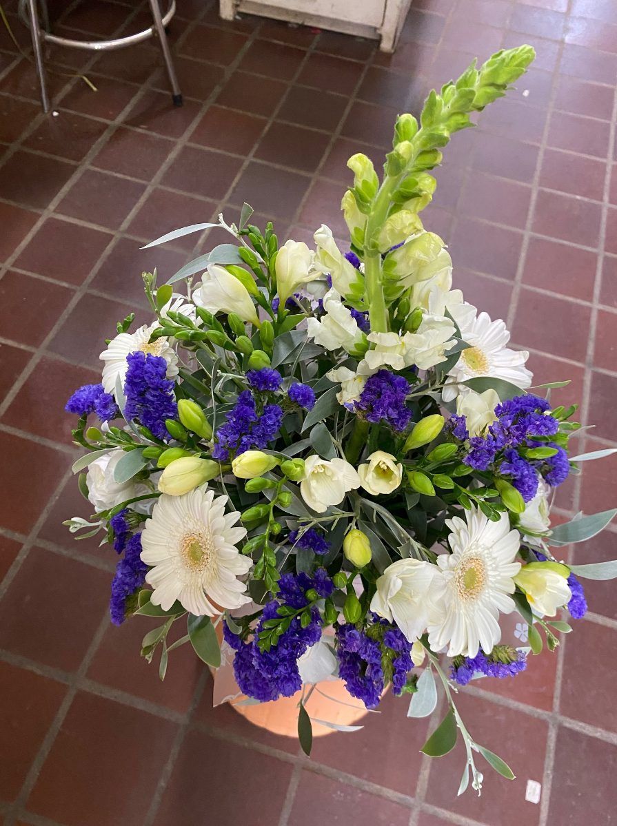 A Vase Filled With Blue and White Flowers is Sitting on a Tiled Floor — Wingham Nursery and Florist PTY Ltd In Forster, NSW