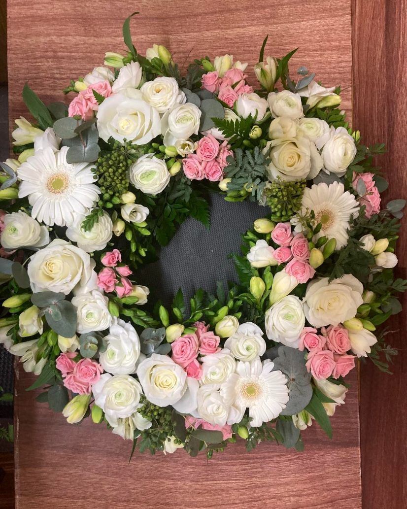 A Wreath of White and Pink Flowers is Sitting on a Wooden Table — Wingham Nursery and Florist PTY Ltd In Wingham, NSW