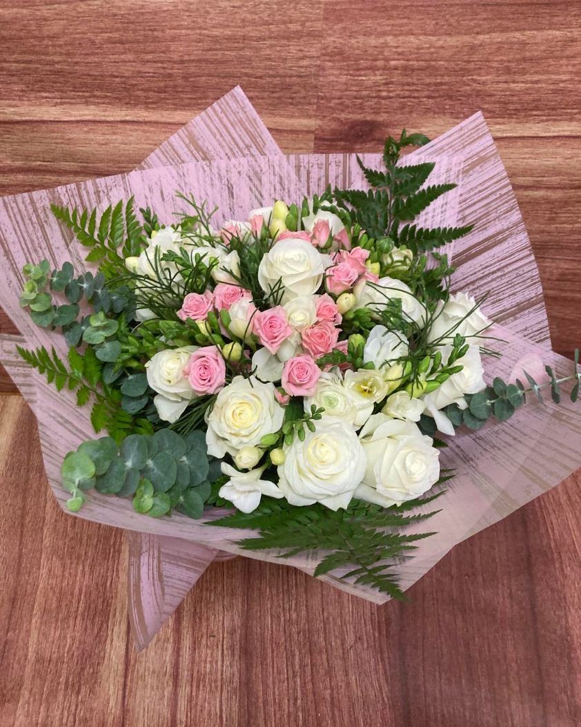 A Bouquet of Flowers Wrapped in Pink Paper is Sitting on a Wooden Table — Wingham Nursery and Florist PTY Ltd In Wingham, NSW