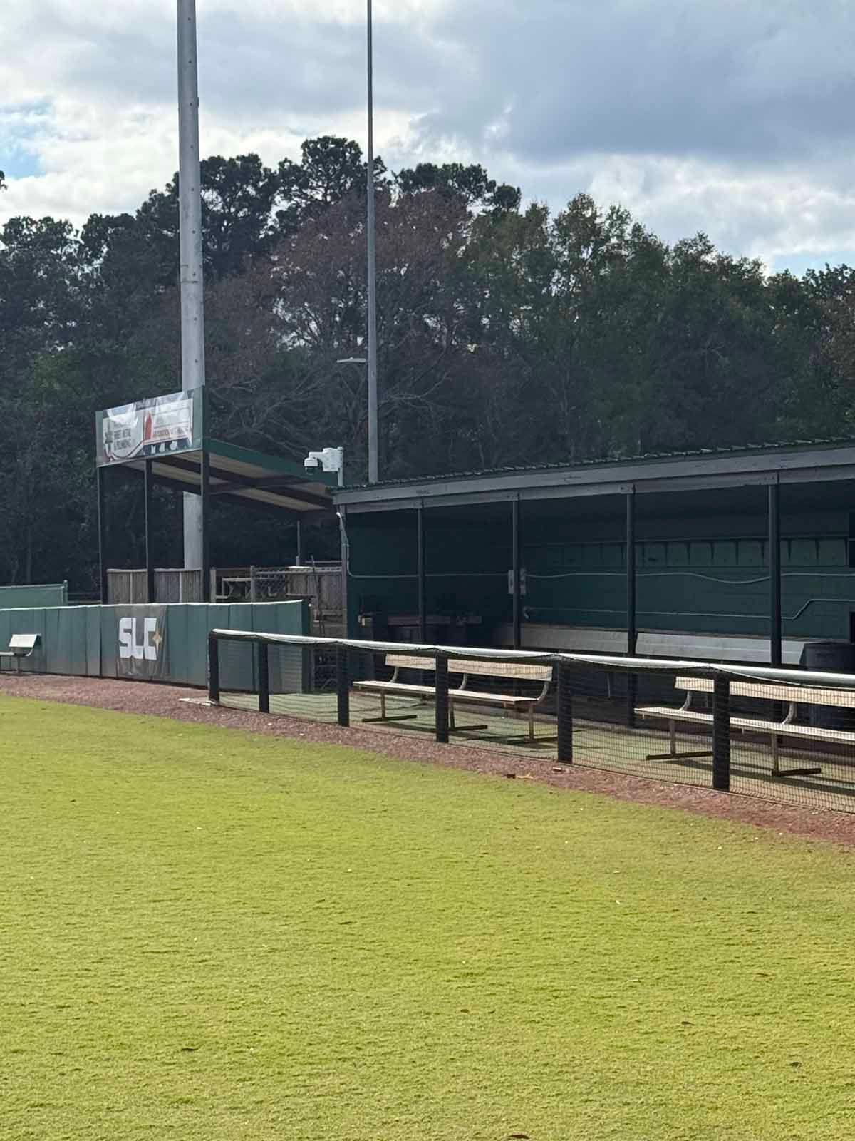 Baseball dugout with green benches and a scoreboard in the background.