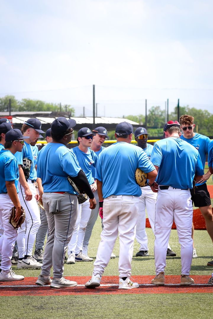 Baseball catcher and pitcher fist bump on a baseball field. Both wear white uniforms with green trim.