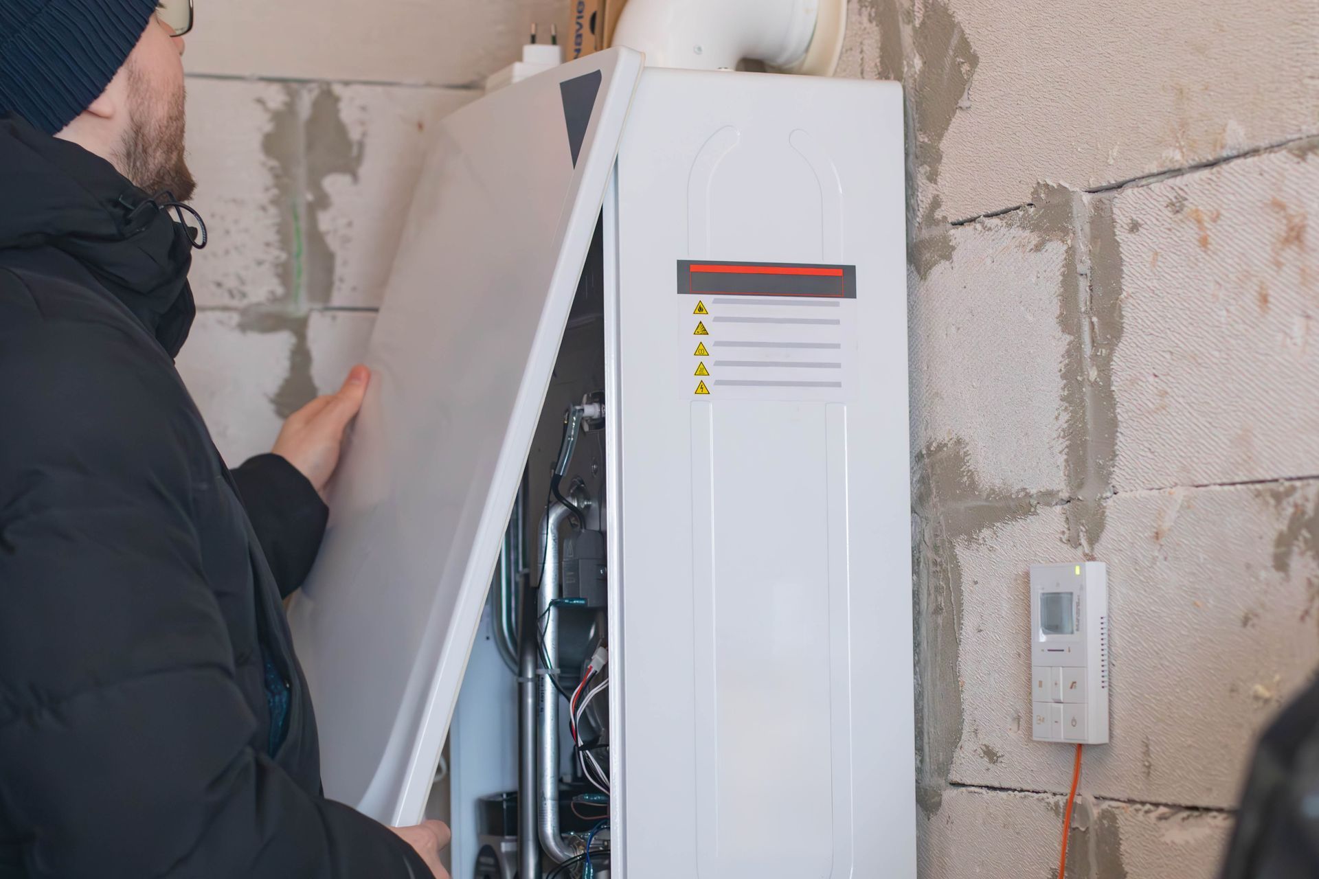 Technician opening a white wall-mounted boiler or HVAC unit in a damaged room