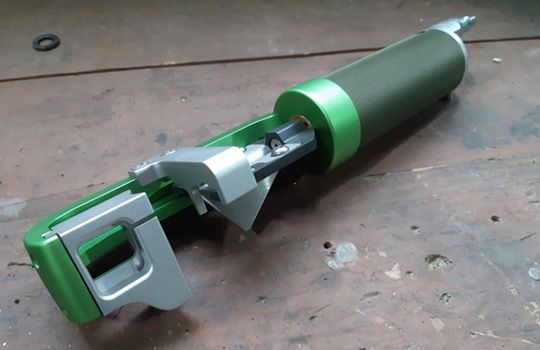 A green and silver tool is sitting on a wooden table